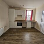 Studio flat eastbourne with kitchen cupboards, cooker, stainless steel sink, door, radiator and wood effect flooring.